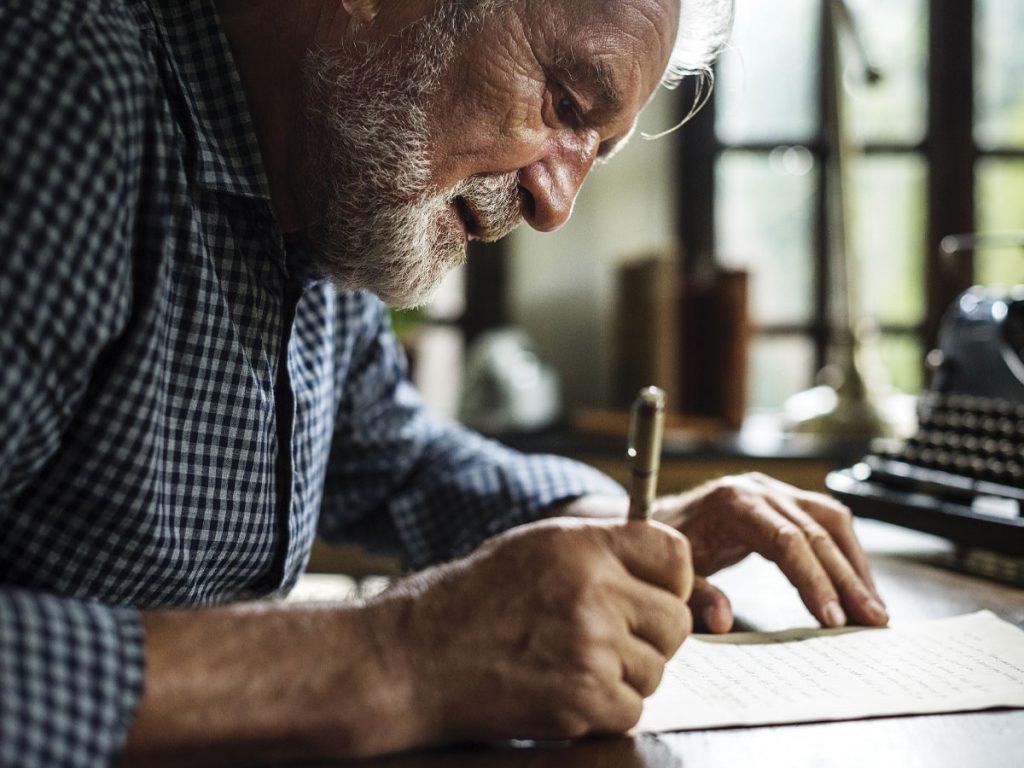 Photo of senior man with beard leaning over and writing on a piece of paper