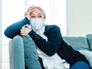 Photo of a senior woman wearing a mask, sitting on a blue couch.