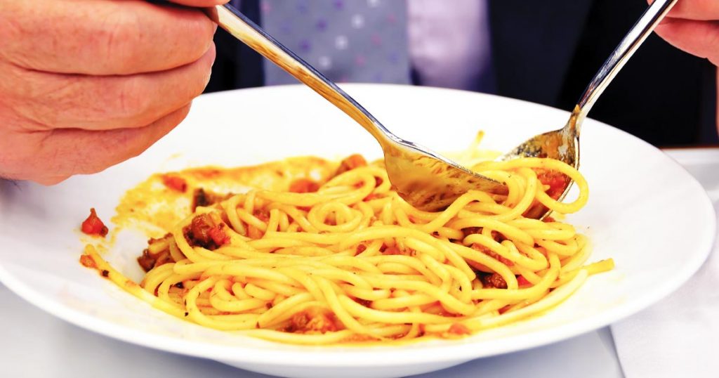 Close-up photo of a senior's hand holding a fork and twirling spaghetti from a pasta bowl.