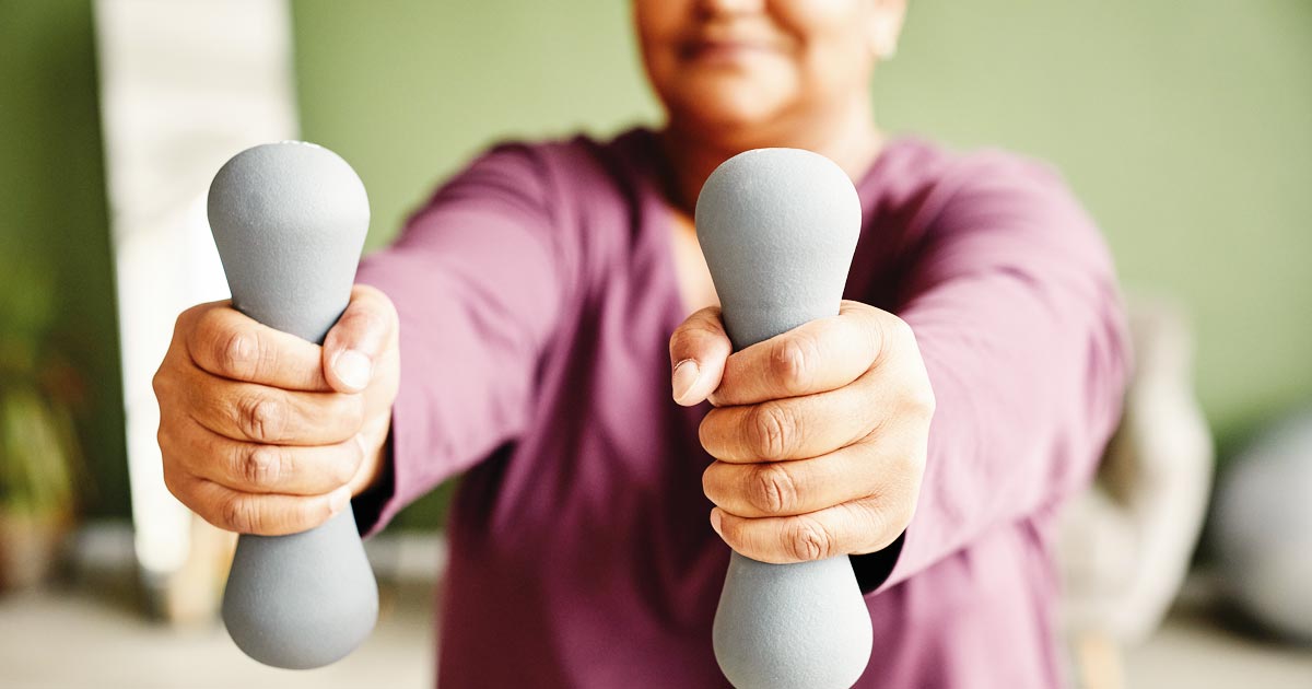 Closely cropped image of a senior woman holding hand-held weights out in front of her.