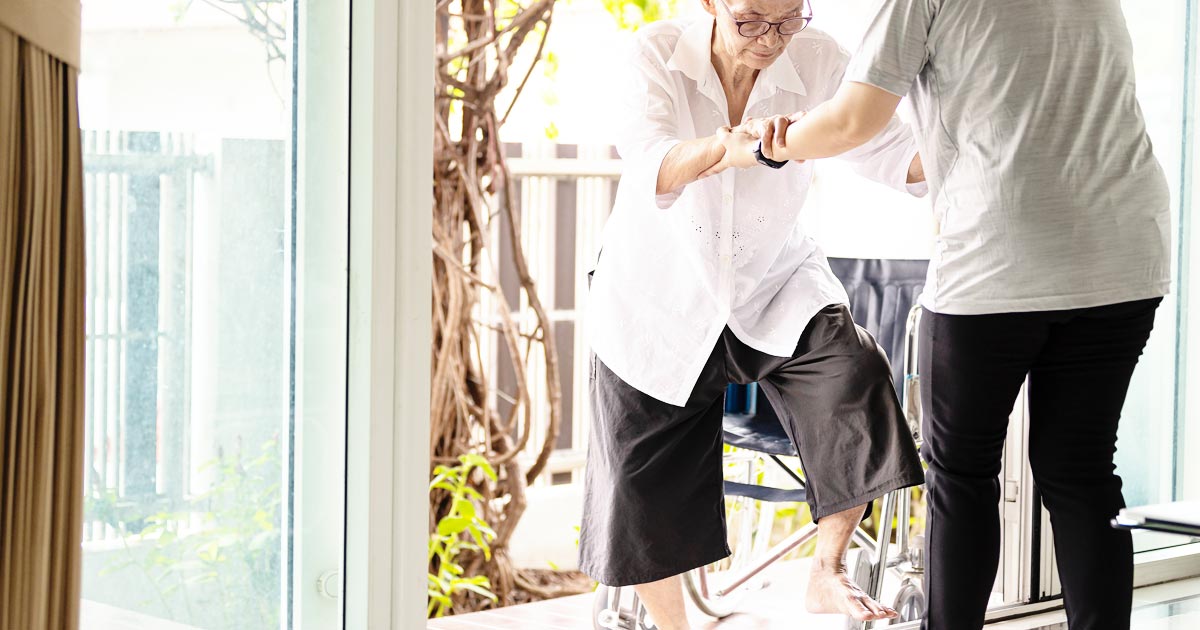 photo of an in-home helper assisting a senior woman over a door stoop