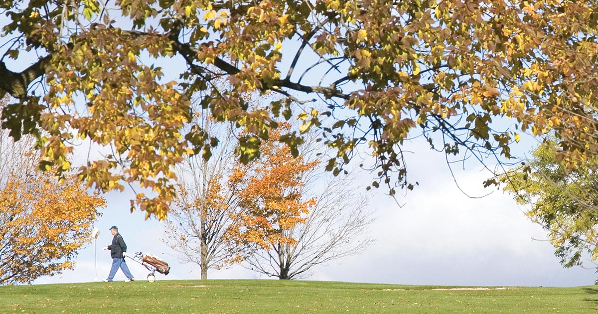 photo of a golfer walking across a golf course in fall