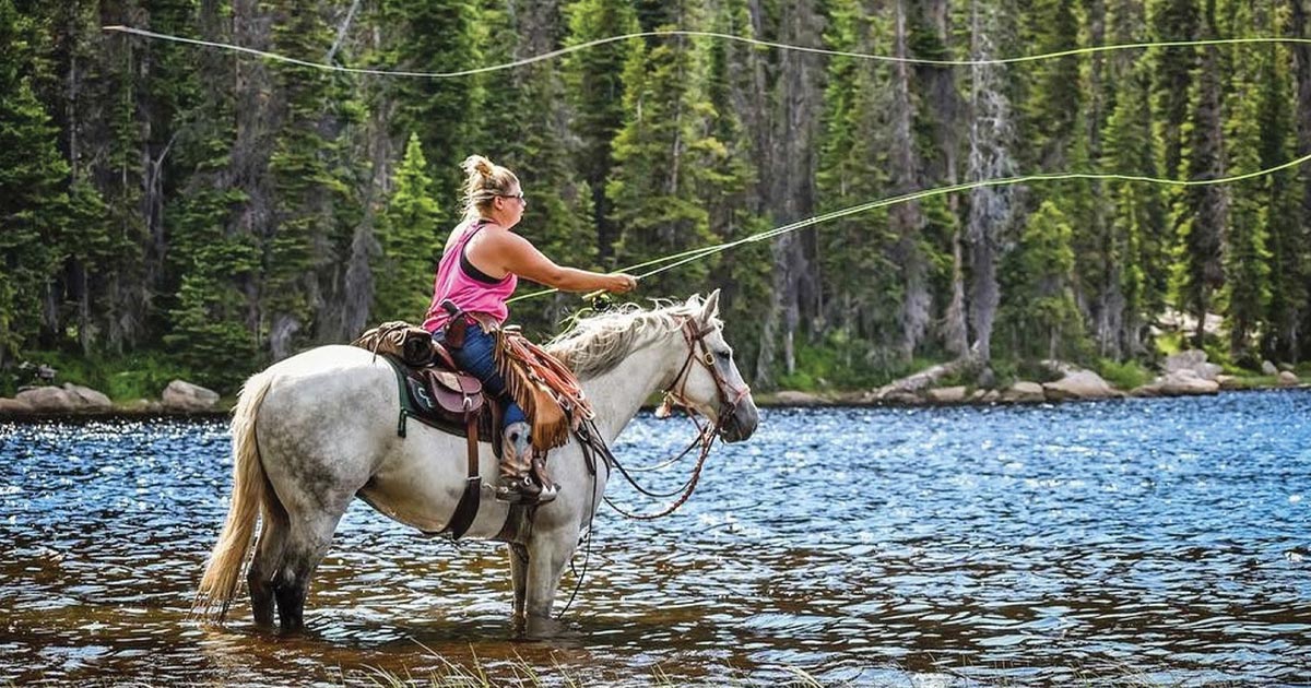 woman sitting on horseback in the middle of a river, casting her fly rod