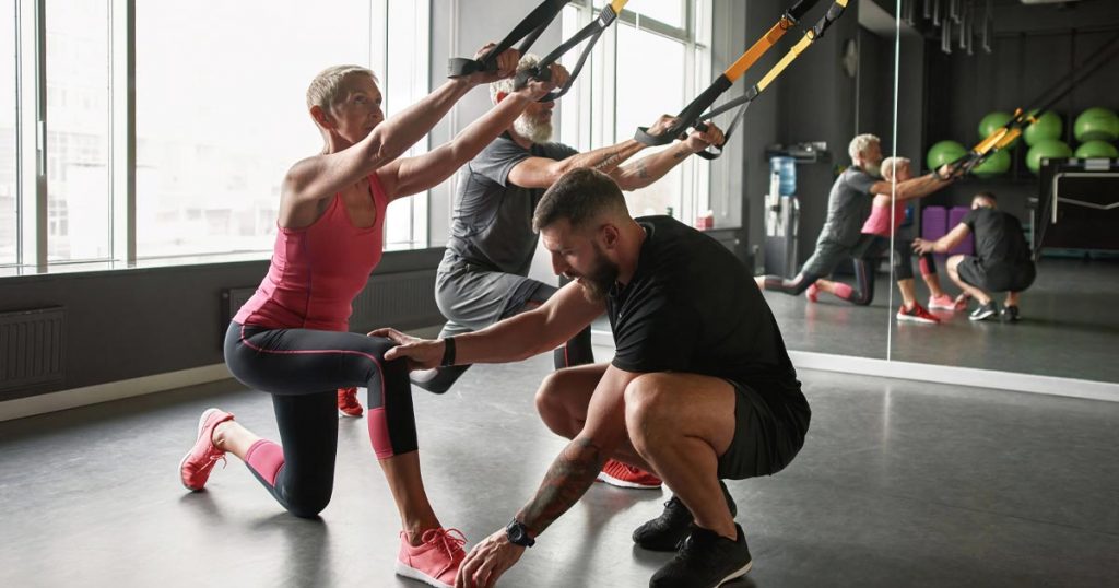 Photo of elder man and woman with a fitness coach at a gym