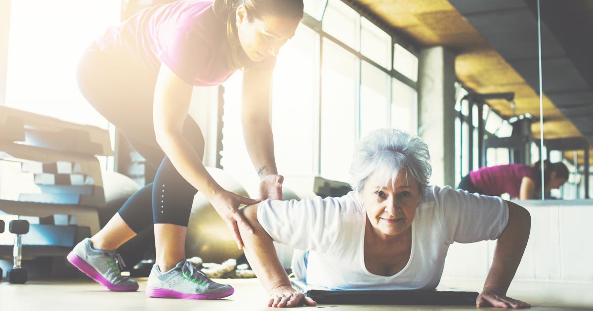 photo of a senior woman at the gym doing pushups with a trainer