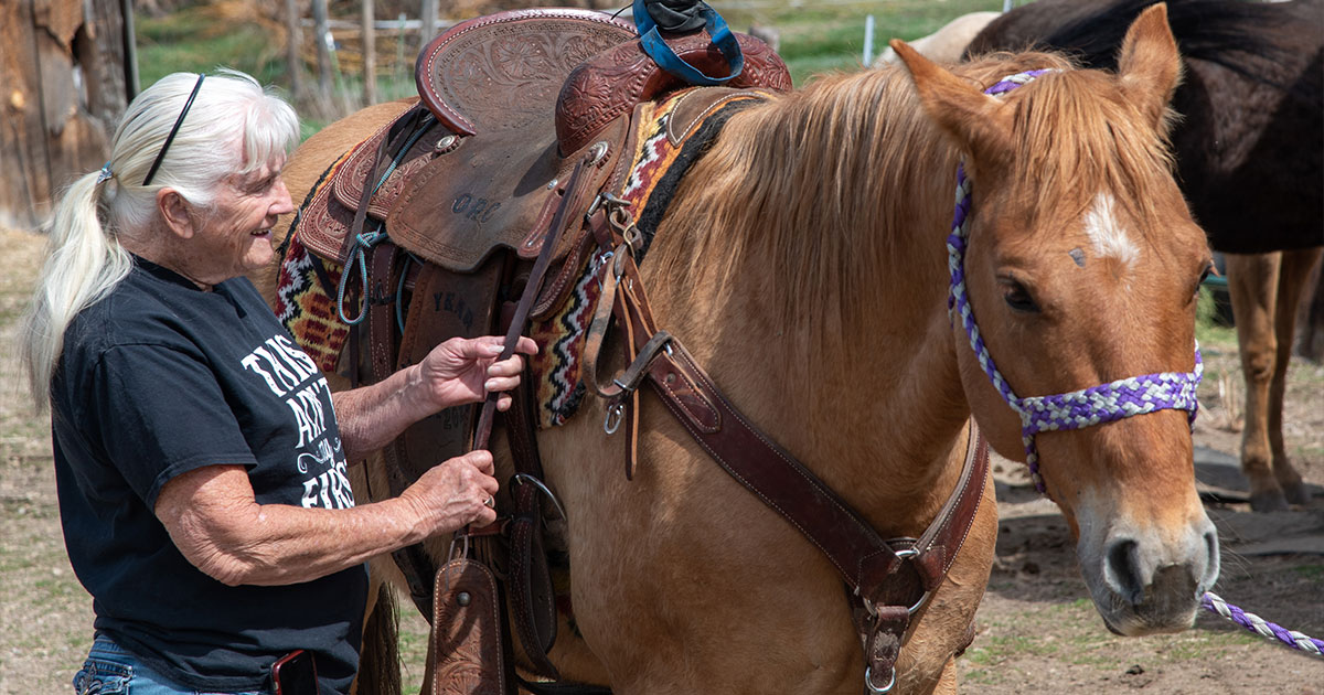 Photo of Jan Youren, Idaho rodeo hall of famer, putting a saddle on her horse.